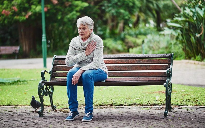 Una mujer sentada en un banco con dolor en el corazón