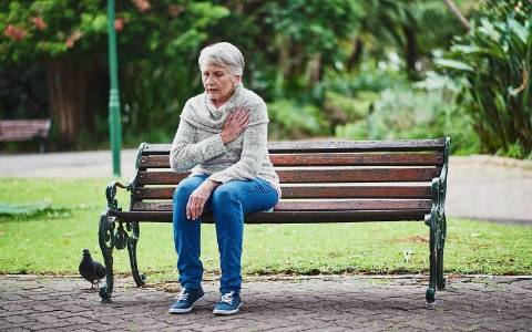 Una mujer sentada en un banco con dolor en el corazón