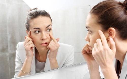 Una mujer joven se mira las ojeras en un espejo